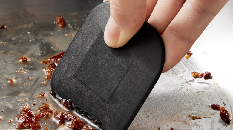 Hand holding pan scraped scarping bits off pan.