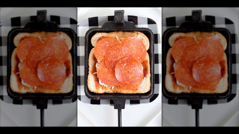 Piece of bread topped with tomato sauce, cheese, and pepperoni in a mountain pie maker