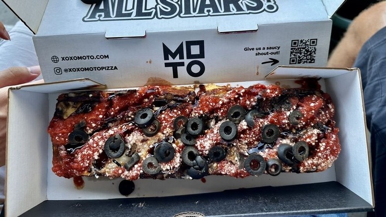 A person holding a slice of Moto Pizza at T-Mobile Park