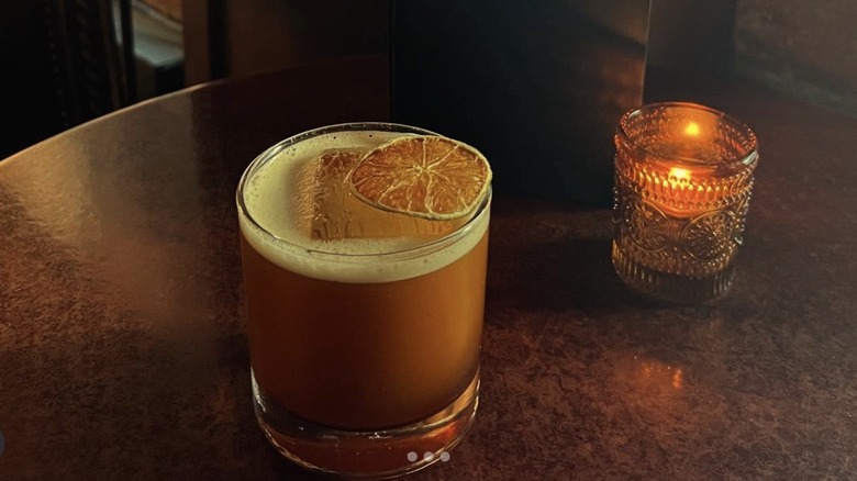 A cocktail garnishes with a candied orange slice and a candle on a table at Bathtub Gin & Co speakeasy in Seattle.