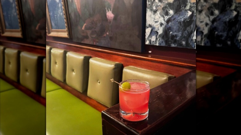 A colorful cocktail sits near green bench seating at The Hideout bar in Seattle.