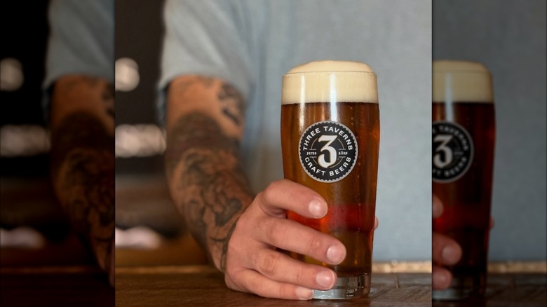 A hand holding a three tavern's beer