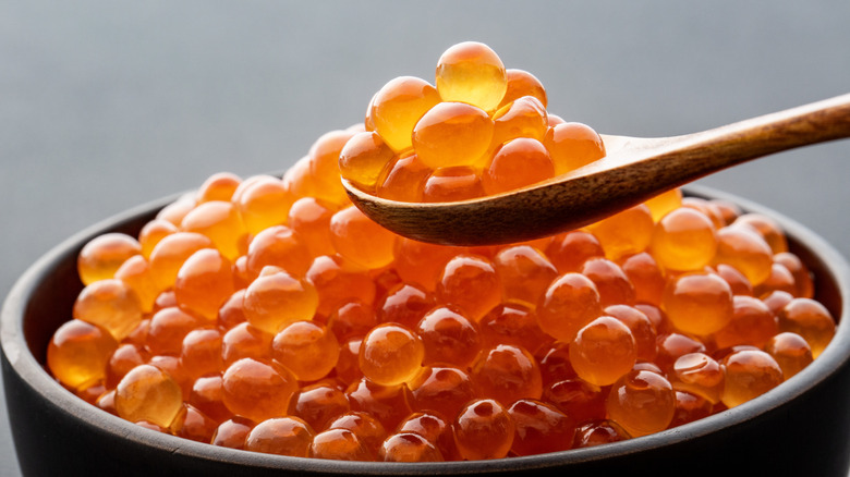 A small bowl of beautiful, bright orange salmon roe with a small wooden spoonfull removed.