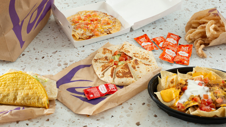 A Taco Bell combo including a Crunchwrap Supreme, a Crunchy Taco, a Mexican pizza, cinnamon twists, nachos, and hot sauce packets