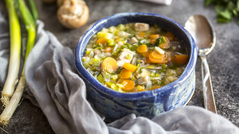 A blue bowl if chicken soup with a spoon and ingredients also arranged in the frame.