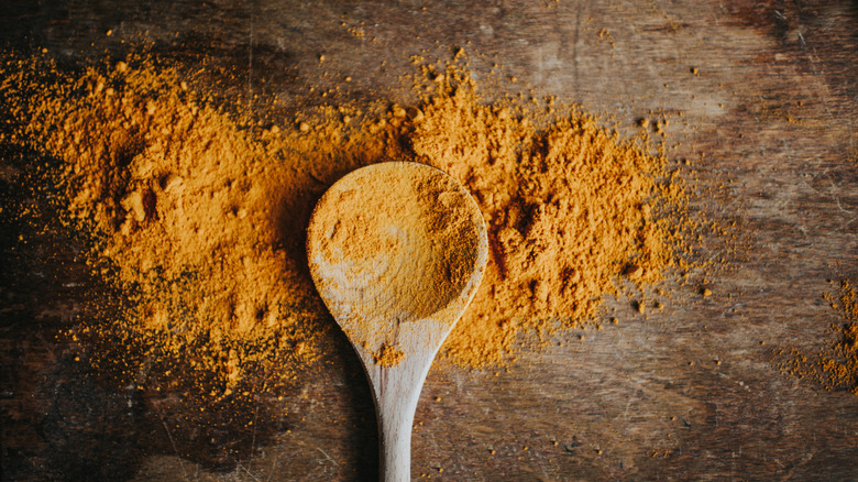 A wooden spoot atop a styled pile of orange turmeric