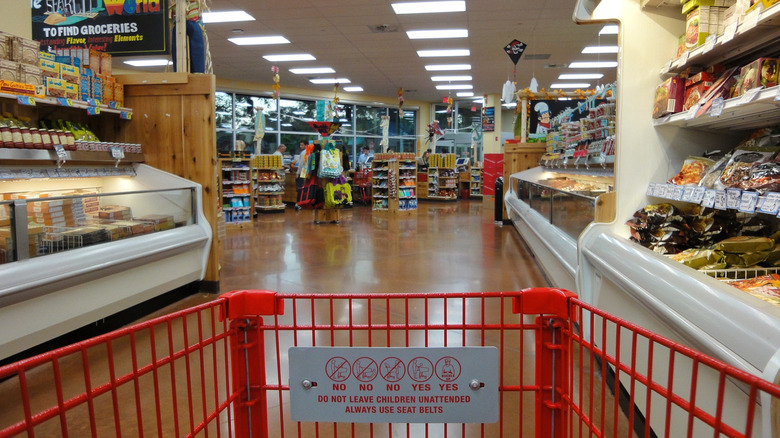 An image of an interior of a grocery store taken from a red shopping cart