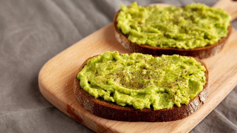 Homemade Avocado Toast with Salt and Pepper on a wooden board, side view.