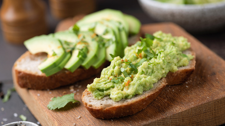 Toast with avocado and seeds on wooden board, closeup view.