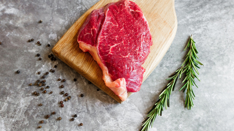 Bright red raw steak on a wooden chopping board with a sprig of rosemary alongside