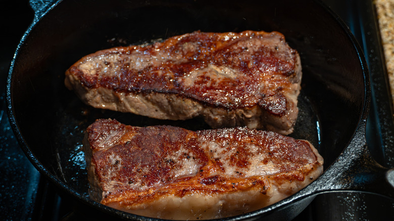 New York strip steaks being seared in a pan
