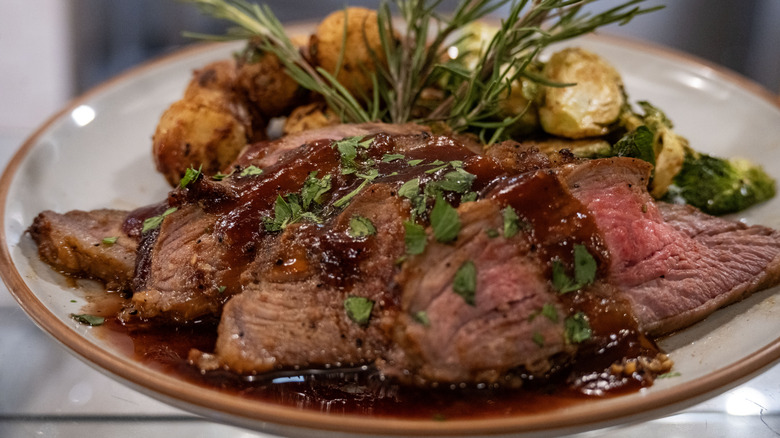 Beef roast on a plate with herbs and a brown sauce