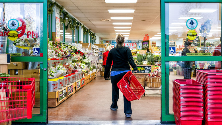 Woman walking into Trader Joe's with handheld basket.