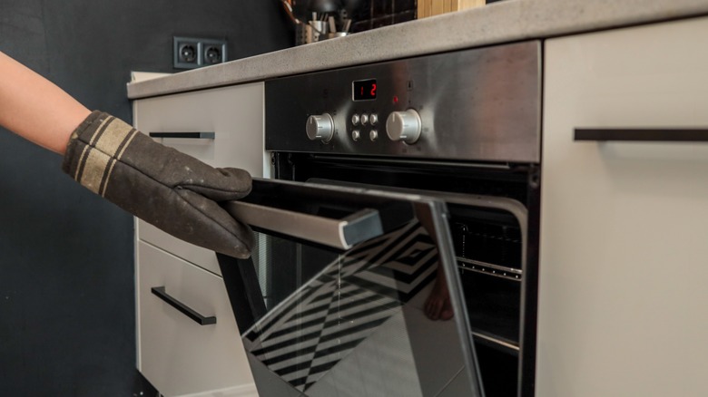 Hand in oven mitt opening door of oven