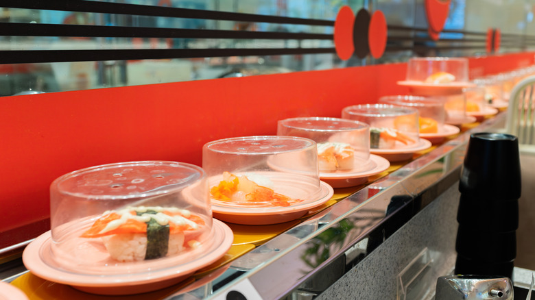 Plates of sushi with a hygienic clear cover lined up neatly at a conveyor belt sushi restaurant