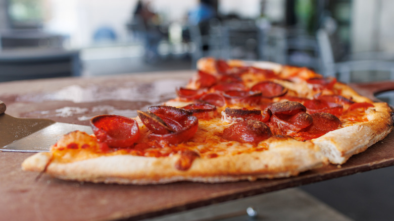 A half leftover, thin-crust pepperoni pizza on a wooden serving platter.