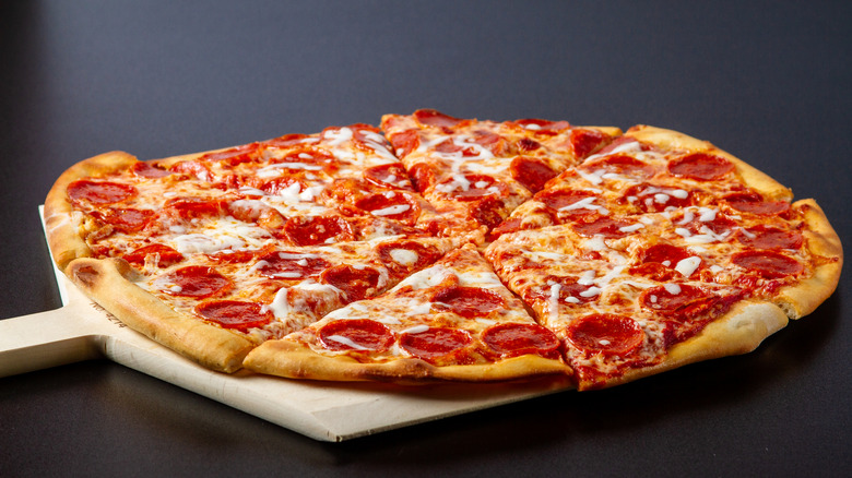 A hot, thin-crust pepperoni pizza, fresh out of the oven on a wooden pizza paddle.