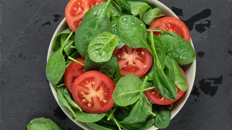 Spinach and tomato salad in a bowl on a gray background.