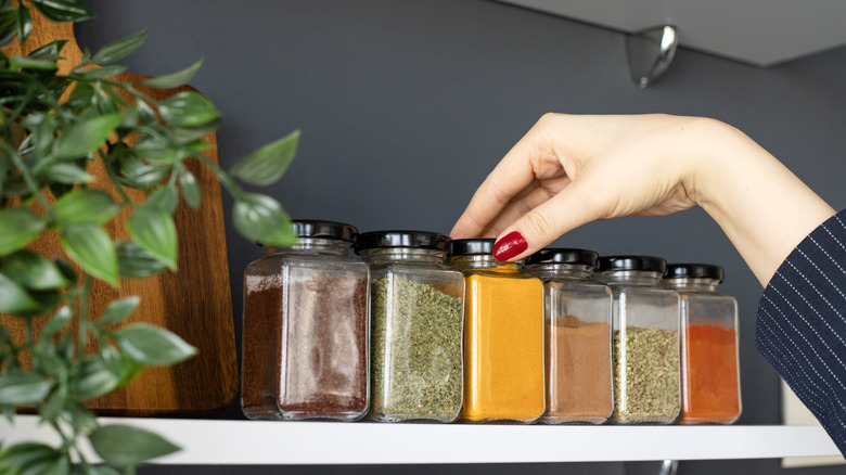 Hand reaching for spice containers on a shelf