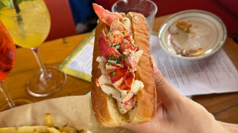 A person holding a lobster roll in front of a table