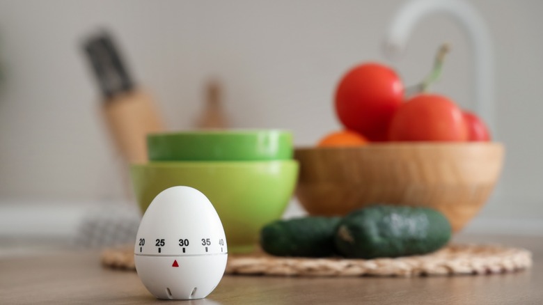 An egg timer on the countertop in front of veggies, knives, and bowls.