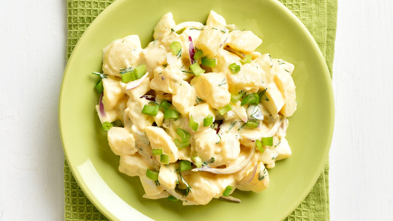 Homemade potato salad with egg, pickle, green onion with mayonnaise and yogurt dressing on green plate on white wooden background. Top view, flat lay