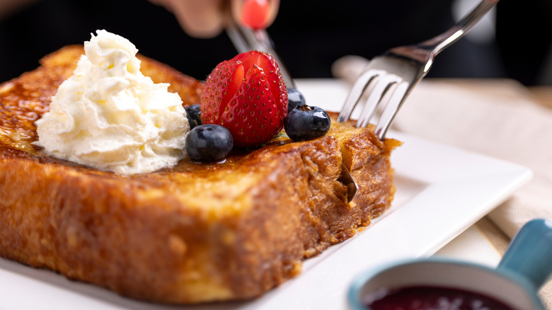 A knife and fork cut into a thick piece of French toast