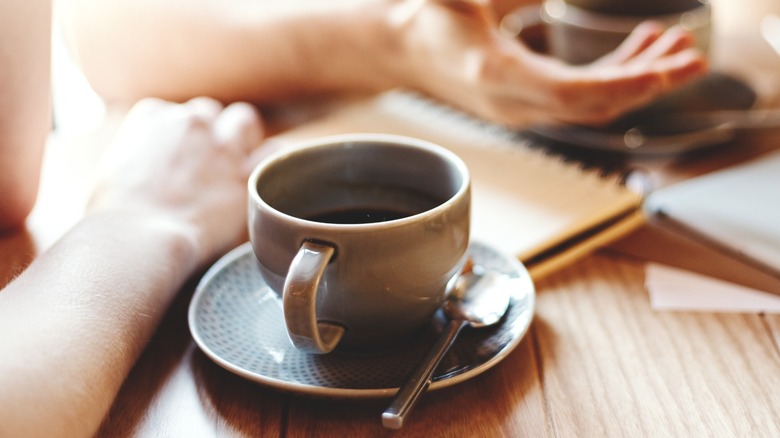 Closeup of mugs of coffee on a table while people talk.