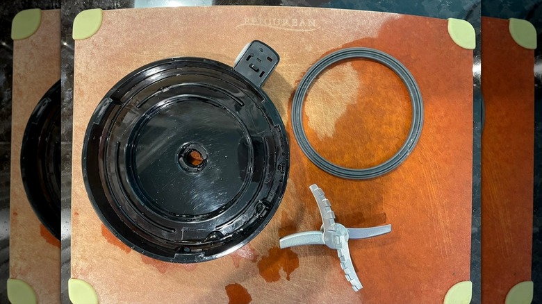 A Ninja Creami lid, blade, and rubber gasket on a cutting board