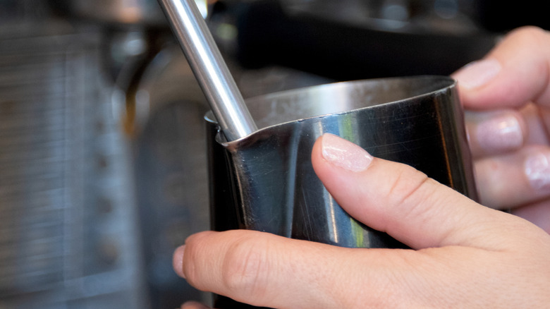 a metal pitcher being held underneath a steam wand
