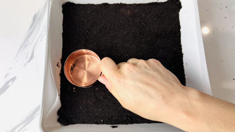 Oreo crust being pressed into baking pan