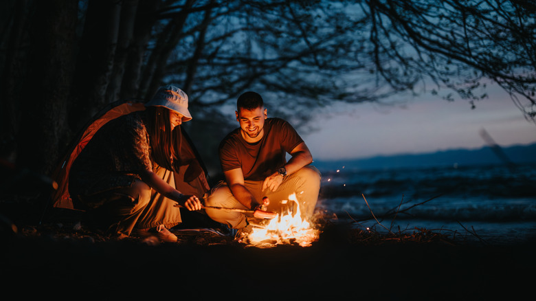 Two people cooking over a campfire