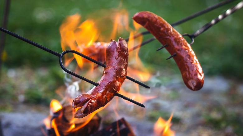 Two roasted hot dogs over a fire