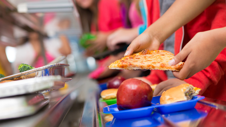 Someone putting a slice of pizza onto a school lunch tray
