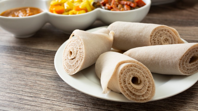Rolled injera on a plate next to bowls of sauce