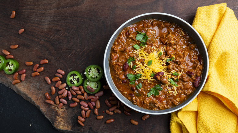 Overhead shot of a bowl of chili alongside beans and a yellow hand towel