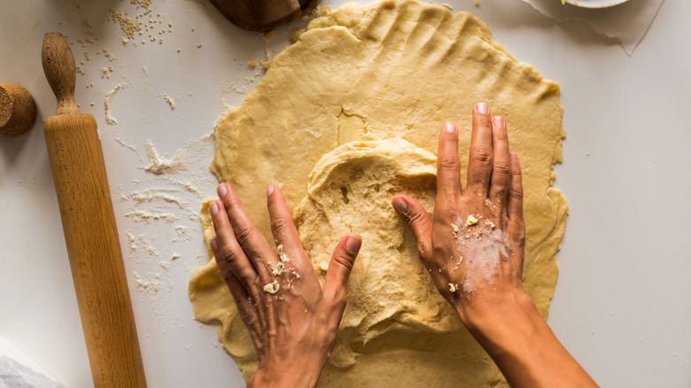 Rolling out pie dough with hands and a rolling pin.