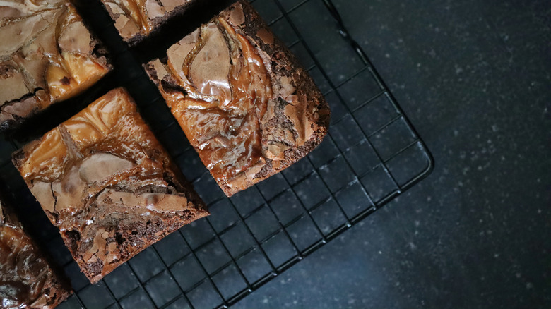 Stock photo showing elevated view of cooling rack of homemade chocolate salted caramel brownies cut into square slices.