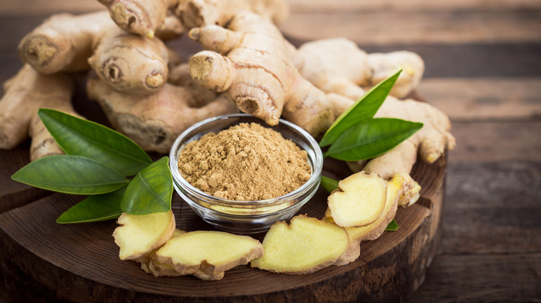 A small bowl of ginger powder is arranged with whole and sliced ginger.