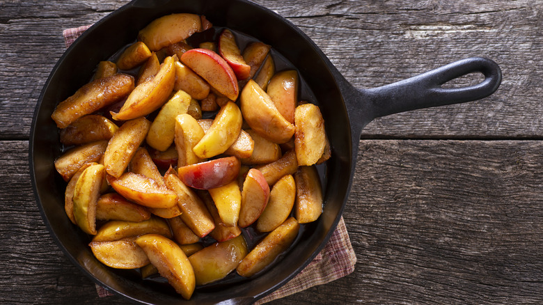 Sliced apples in a skillet on a wooden table.
