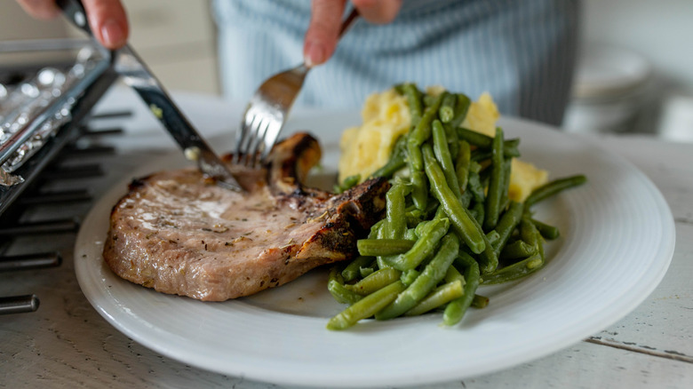 Person eating pork chop with mashed potatoes.