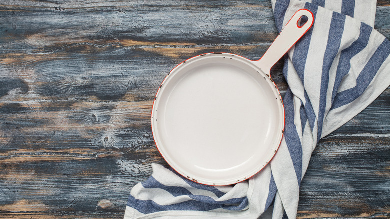 A white enamal cast iron pan on wooden background with a towel