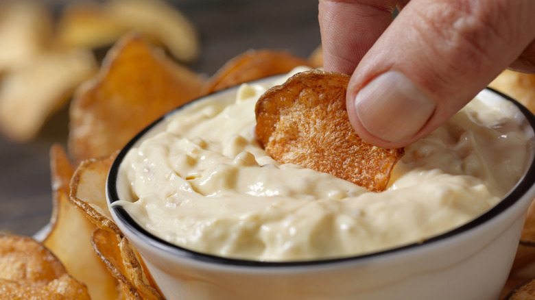Hand dipping a potato chip into French onion dip.