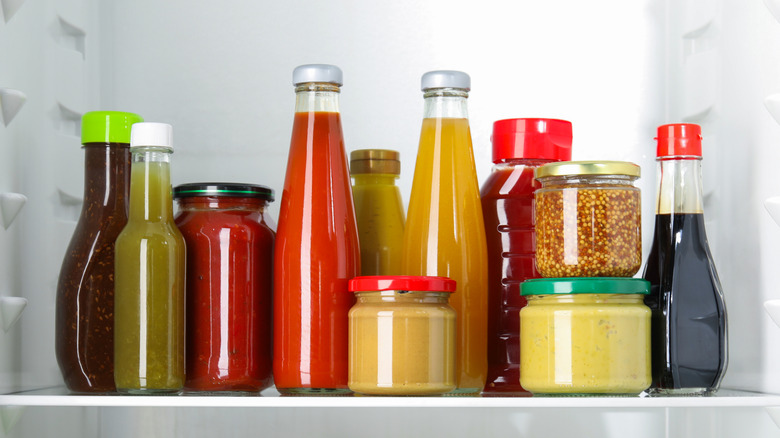Assorted condiment bottles in a refrigerator with vegetables on the shelf below