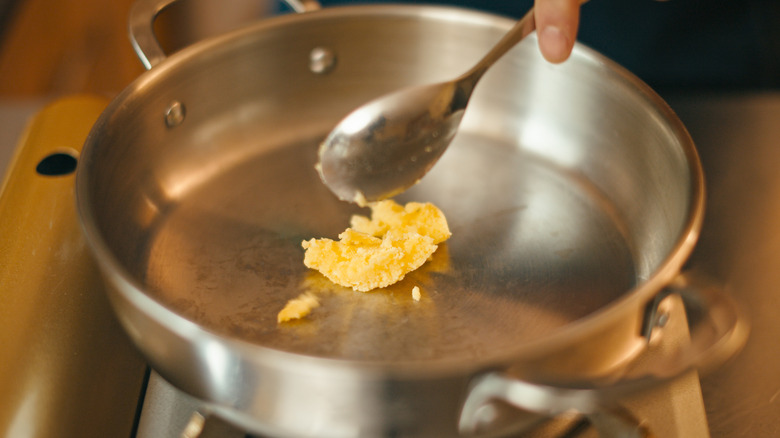 An individual adding ghee to a hot pan.
