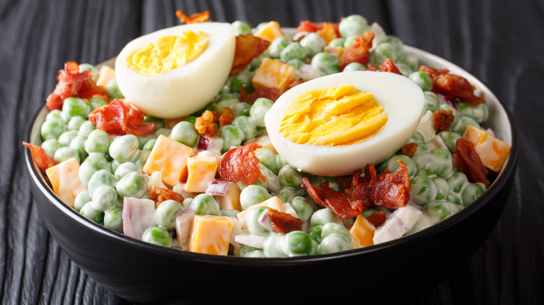 A bowl of pea salad topped with hard-boiled eggs on a wooden table.