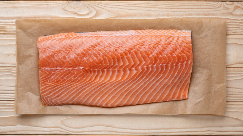 Raw salmon filet on parchment paper on a slatted wood surface