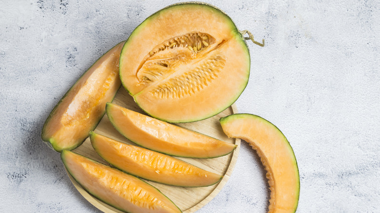 Sliced cantaloupe pieces and a cantaloupe half sitting on a cutting board