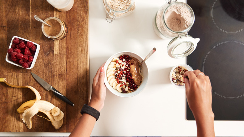 An over head shot of person preparing breakfast bowl with berries, oats, nut butter and seeds
