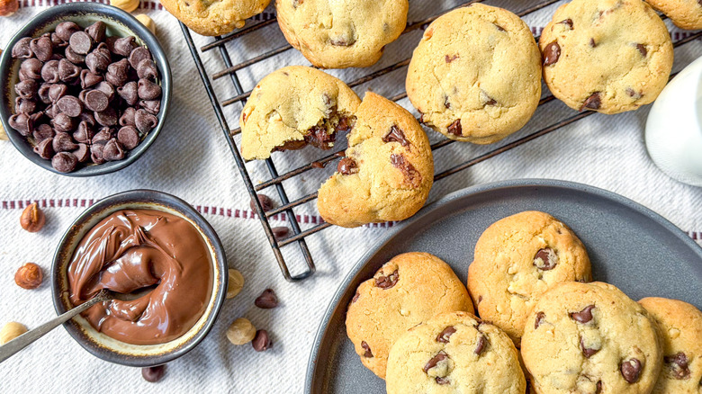 Nutella-stuffed chocolate chip cookies on plate and cooling rack with bowl of chocolate chips and Nutella